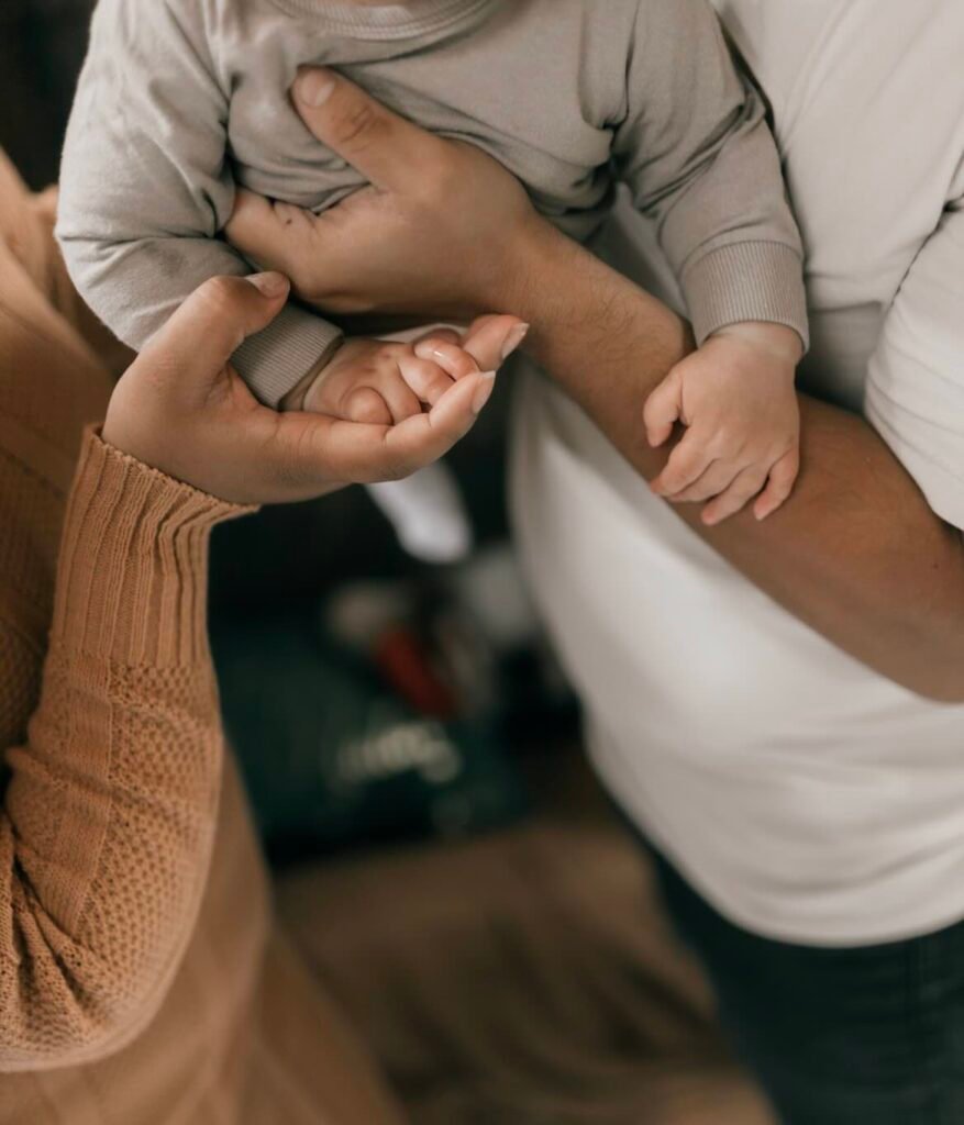 Padre sosteniendo con ternura la mano de su bebé recién nacido, junto a la mano de su pareja, en referencia a la fertilidad durante el tratamiento con finasteride o dutasteride
